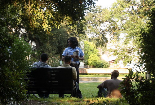 Detective Claudia Bruce hands out CrimeStoppers flyers to a group of men sitting in Coliseum Square during an anti-crime march in July 2013.  (UptownMessenger.com file photo by Robert Morris)