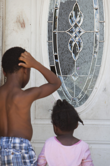 Children look at broken glass on the front door of the home where a shooting claimed the life of an eleven year old girl. (Sabree Hill, UptownMessenger.com)