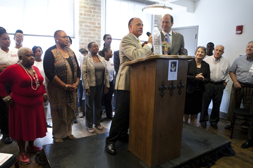 Founder Craig Cuccia stands next to CEO R. Glen Armantrout, III as he gets ready to bless a cross with water that he brought back from the Jordan River. The cross was later hung over the Cafe Reconcile doorway. (Sabree Hill, UptownMessenger.com)
