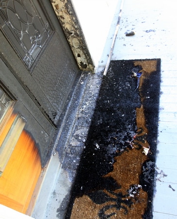 The front door of a home in the 2300 block of Octavia Street remains charred on Tuesday afternoon, with tatters of the American flag that was also burned. (Robert Morris, UptownMessenger.com)