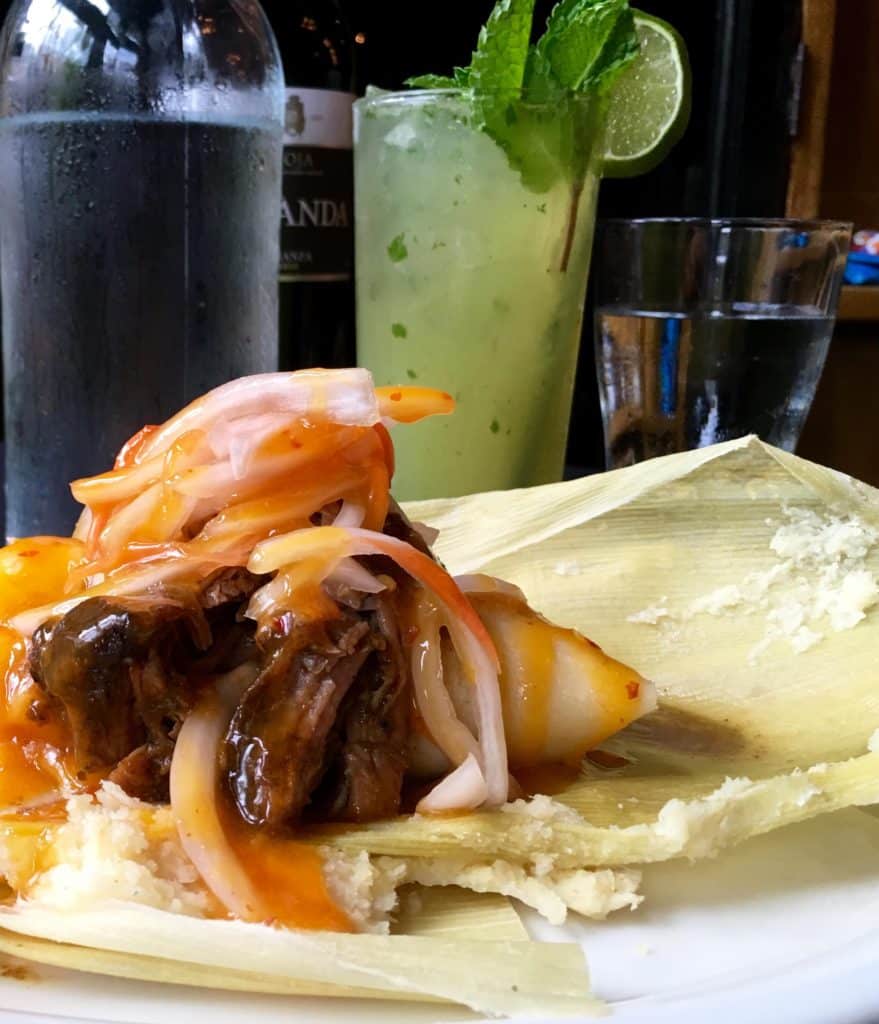 Tamal Criollo or Cuban Tamal of Sweet Corn and Roasted Pork topped with escaveche onions wrapped in corn husk; Classic Mojito (Kristine Froeba)