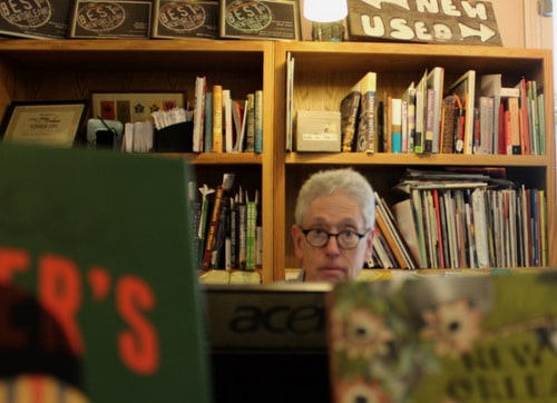 Gladin Scott looks up behind a pile of books on Oct. 24, 2016. Behind him are sticky notes with numbers of frequent customers and authors that he has compiled from his years as owner. (Photo by Dannielle Garcia, Loyola Student News Service).